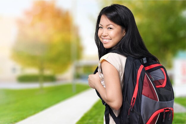 Junge asiatische Studentin mit Rucksack auf verschwommenem Parkhintergrund