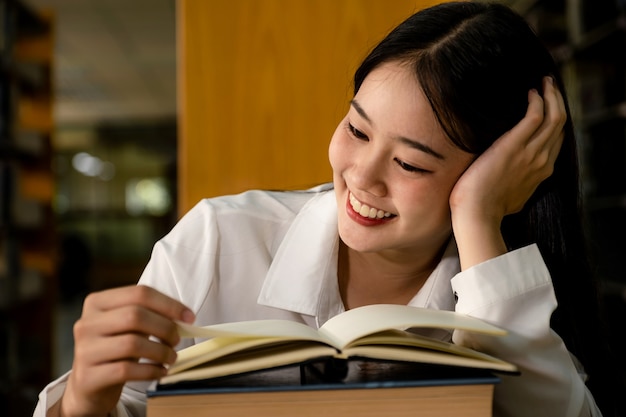 Junge asiatische Studentinnen lesen Buchrecherchen und lernen aus Lehrbüchern in der Universitätsbibliothek.