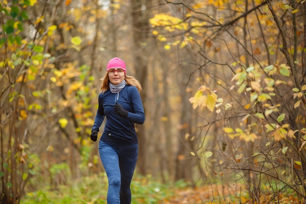 Junge athletische Frau, die im bunten Herbstwald läuft. Konzept für Gesundheit und aktives Leben