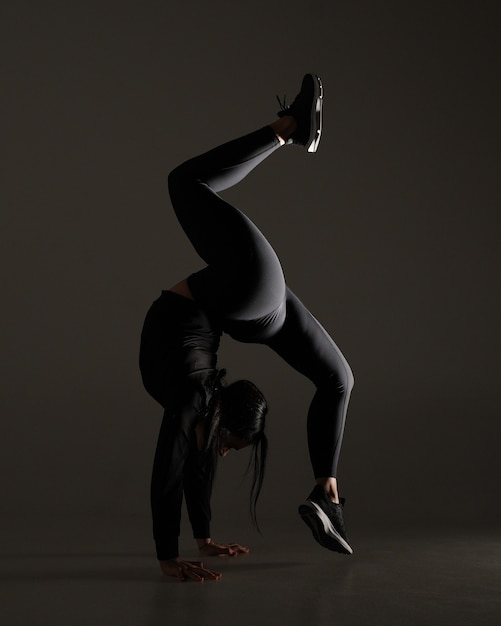 Junge athletische Frau macht Yoga und Gymnastik Dehnübungen auf dunklem dramatischem Hintergrund mit ...
