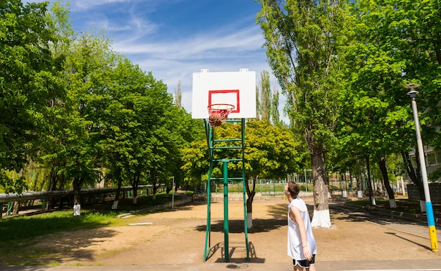 Junge athletische Mann beobachten erfolgreichen Schuss mit Ball im Netz auf Basketballplatz im üppigen grünen Park