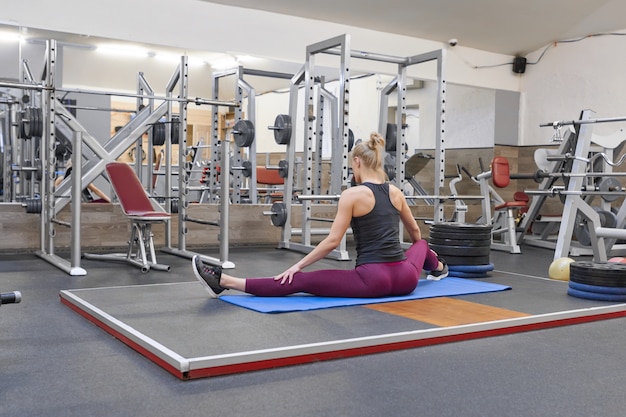 Junge athletische muskulöse frau, die training in der turnhalle ausdehnend tut