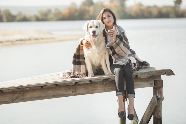 Junge attraktive Frau, die am Pier mit ihrem Hund sitzt. Beste Freunde im Freien