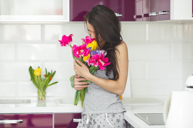 Junge attraktive Frau, die Blumen hält. Dame in der Küche mit Tulpen. Hausfrau morgens, die auf der Hauptküche steht.