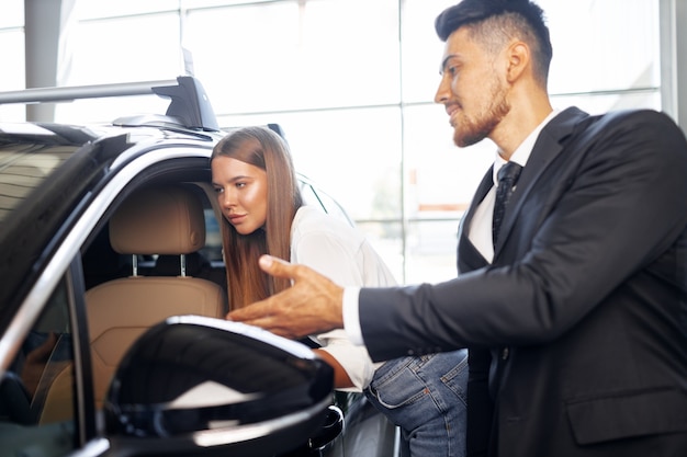 Junge attraktive Frau, die ein neues Auto in einem Autoausstellungsraum sucht