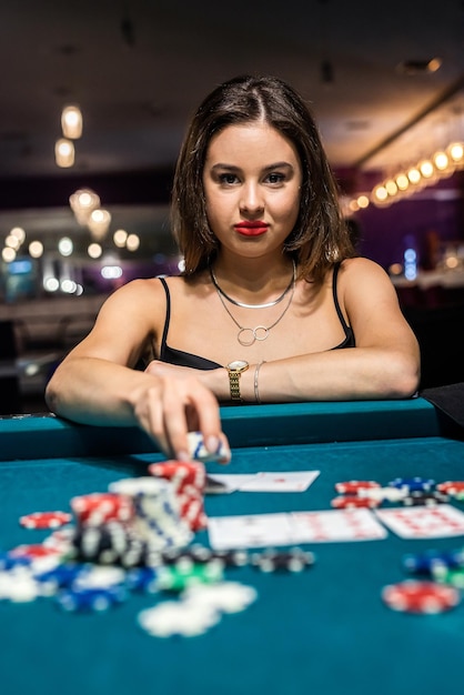 Junge attraktive Frau, die Poker am Tisch mit Stapeln von Chips und Karten spielt