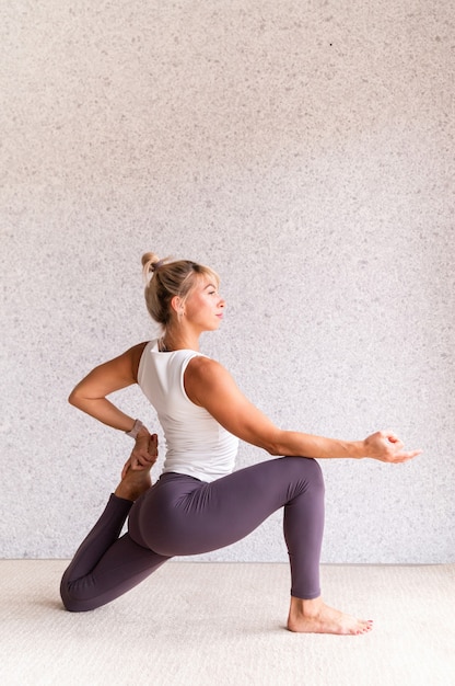 Junge attraktive Frau, die Yoga praktiziert, während sie Sportkleidung drinnen trägt