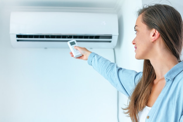 Foto junge attraktive frau, die zu hause fernbedienung für anpassungsklimaanlagentemperatur im raum verwendet.