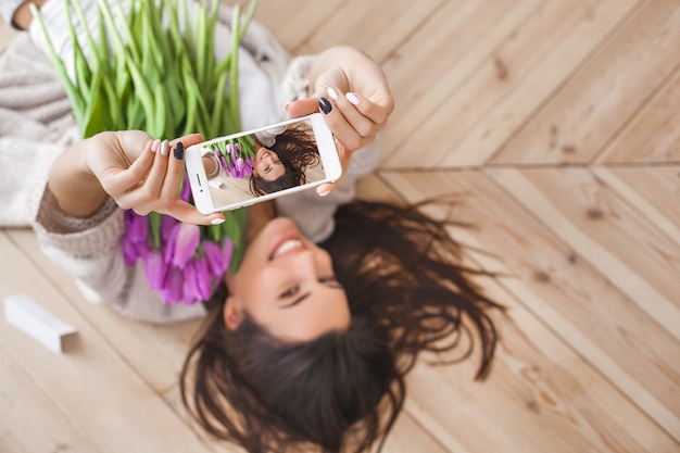 Junge attraktive Frau, die zuhause selfie mit Blumen macht