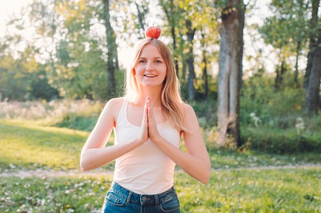 Junge attraktive Frau im Freien, die roten Apfel auf ihrem Kopf hält und an etwas auf der Unschärfennaturoberfläche denkt