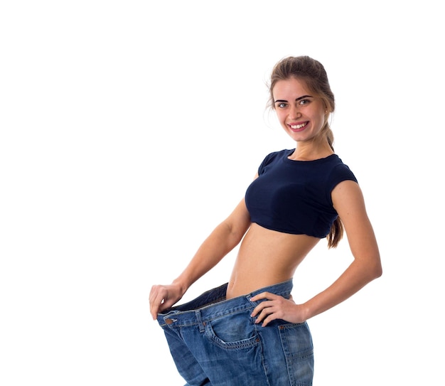 Junge attraktive Frau in blauem Oberteil und viel größeren Jeans im Studio