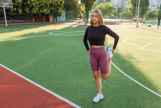 Junge attraktive Frau in Sportbekleidung beim Aufwärmen vor dem Training, Beine im Stadion dehnen. Gesundes Lebensstilkonzept. Training im Freien