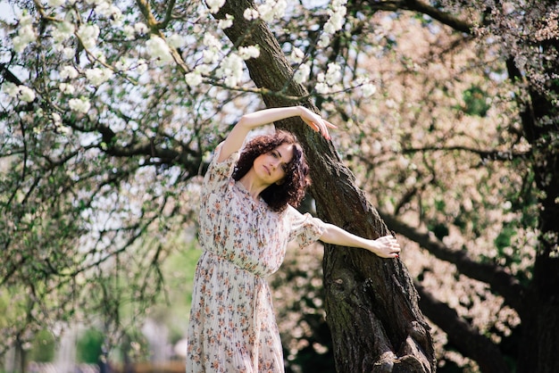 Junge attraktive Frau mit dem lockigen langen Haar, das im blühenden Garten des Frühlings, Apfelbäume aufwirft