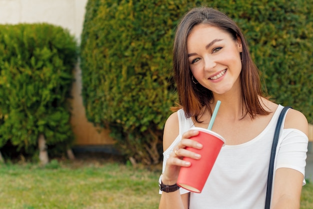Junge attraktive Frau mit einem Getränk in einer Straße an einem sonnigen Tag