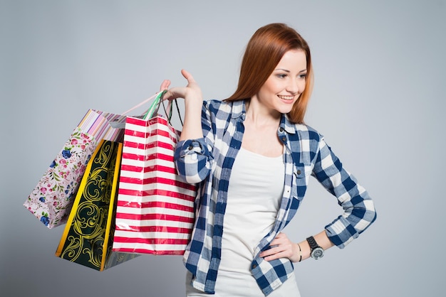 Junge attraktive lächelnde Frau mit vielen farbigen Einkaufstaschen auf Grau. Frau beim Einkaufen