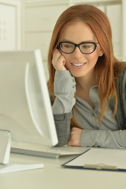 Junge attraktive rothaarige Frau mit Brille, die am Computer arbeitet