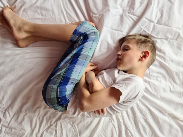 Junge auf dem Bett mit Bauchschmerzen in der Nähe