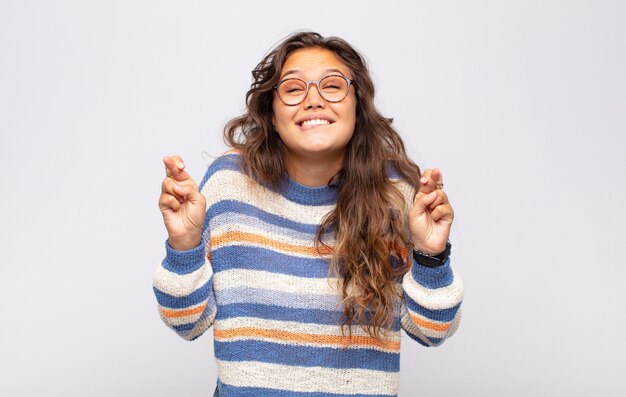 Junge ausdrucksstarke Frau mit Brille posiert auf weißer Wand