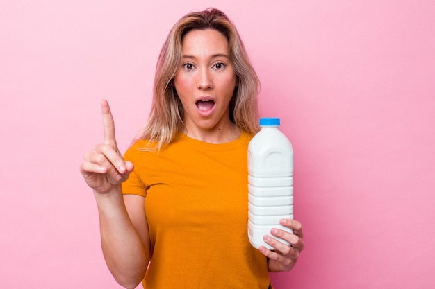 Junge australische Frau, die eine Flasche Milch lokalisiert auf rosa Hintergrund hält eine Idee, Inspirationskonzept hält.