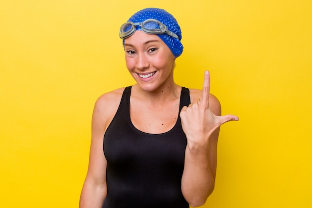 Junge australische Schwimmerfrau lokalisiert auf gelbem Hintergrund, der mit dem Finger auf Sie zeigt, als ob die Einladung näher kommt.