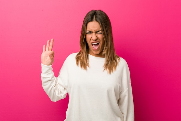 Junge authentische charismatische echte Menschen Frau gegen eine Wand zwinkert ein Auge und hält eine okay Geste mit der Hand.