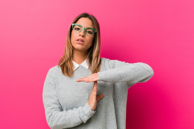 Junge authentische charismatische wirkliche Leutefrau gegen eine Wand, die eine Auszeitgeste zeigt.