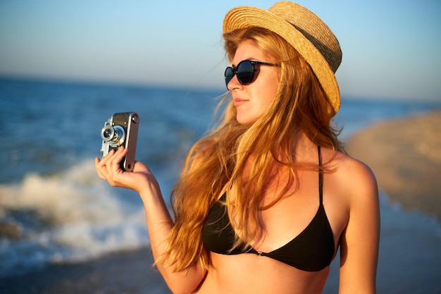 Junge authentische Frau mit Vintage-Retro-Filmkamera, die im Sommerurlaub den tropischen Strand genießt