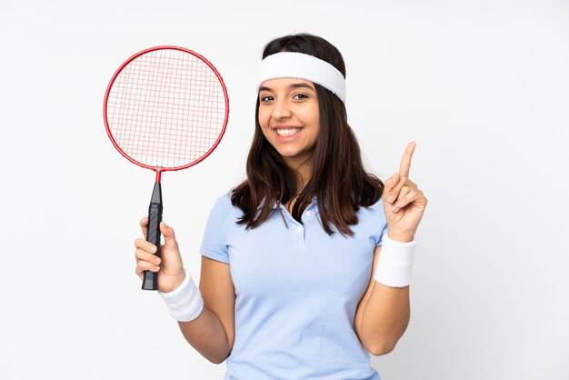 Junge Badmintonspielerfrau über der weißen Wand, die einen Finger im Zeichen des Besten zeigt und anhebt