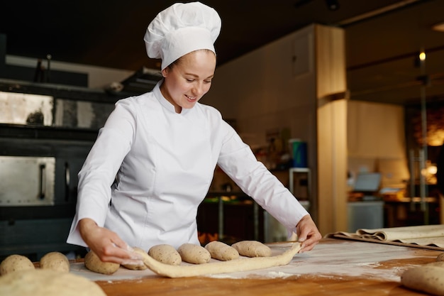 Junge Bäckerin, die in der Bäckerei arbeitet und Baguettes aus rohem Teig formt