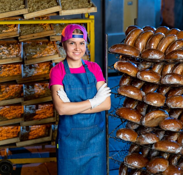 Junge Bäckerin mit verschränkten Armen in der Nähe von Regalen mit frisch gebackenem Brot beim Backen