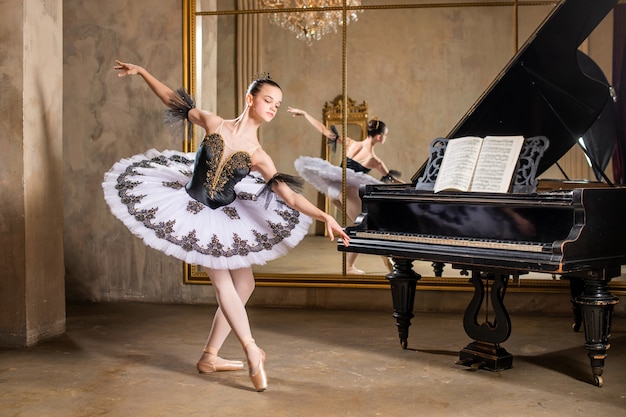 Junge Ballerina in einem weißen Tutu, das auf einem schönen alten Klavier in einem Vintagen Innenraum tanzt