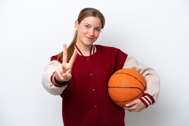 Junge Basketballspielerfrau lokalisiert auf dem weißen Hintergrund, der Siegeszeichen lächelt und zeigt