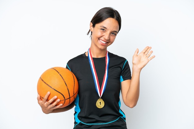 Junge Basketballspielerfrau lokalisiert auf weißem Hintergrund, der mit der Hand mit glücklichem Ausdruck salutiert