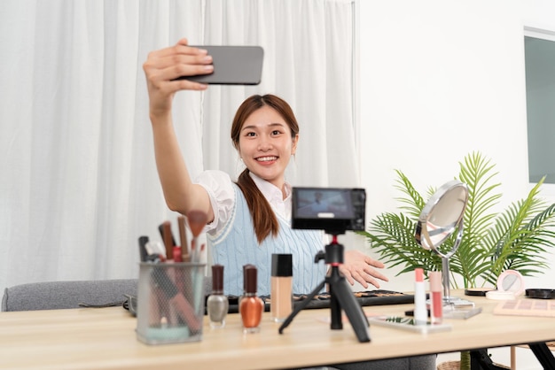 Junge Beauty-Influencerin mit Smartphone zum Selfie mit Beauty-Equipment und Make-up-Accessoires