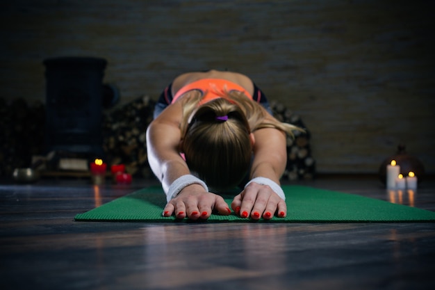 Junge begeisterte Frau, die ihren Rücken auf der Yogamatte biegt und Yoga-Asana mit Kerzen auf dem Hintergrund praktiziert