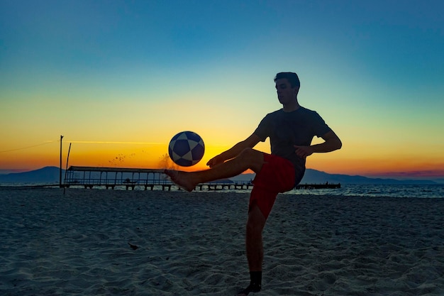 Junge beim Sport mit Ball am Strand bei vollem Sommersonnenuntergang an der brasilianischen Küste