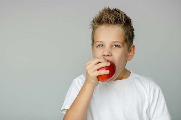 Junge beißt roten Apfel und hält Frucht mit einer Hand