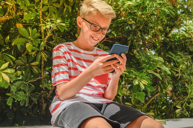 Junge benutzt ein Handy, während er auf der Terrasse des Gebäudes sitzt