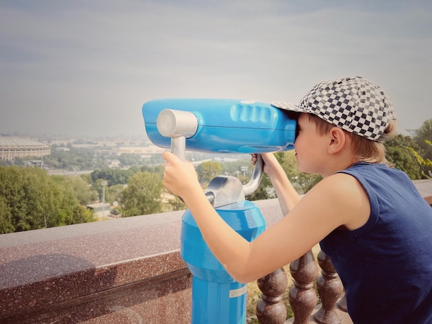 Junge beobachtet Stadtpanorama durch stationäres Fernglas