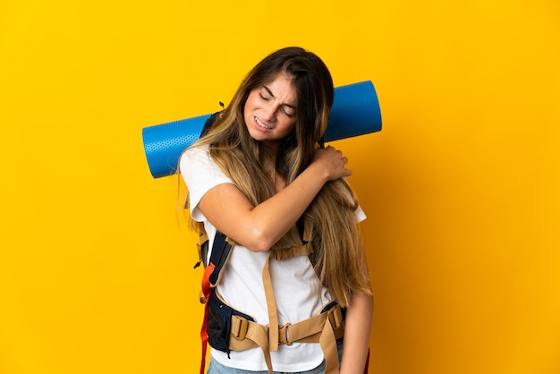 Junge Bergsteigerfrau mit einem großen Rucksack, der auf Gelb isoliert ist und unter Schmerzen in der Schulter leidet, weil sie sich bemüht hat