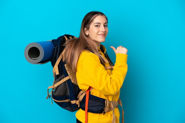 Junge Bergsteigerfrau mit einem großen Rucksack lokalisiert auf blauer Wand stolz und selbstzufrieden