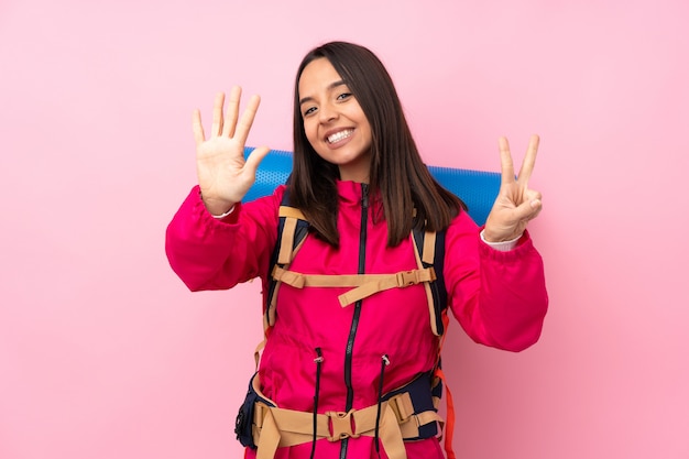 Junge Bergsteigerfrau mit einem großen Rucksack über isolierter rosa Wand, die sieben mit den Fingern zählt