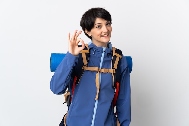 Junge Bergsteigerfrau über lokalisiertem Hintergrund, der ok Zeichen mit den Fingern zeigt