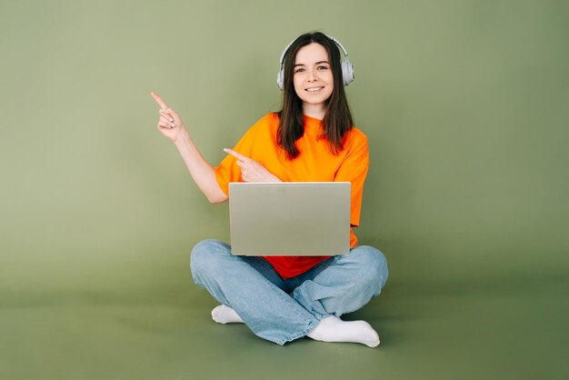 Junge berufstätige Frau arbeitet selbstbewusst am Laptop und zeigt auf leeren Platz für Text und Werbung