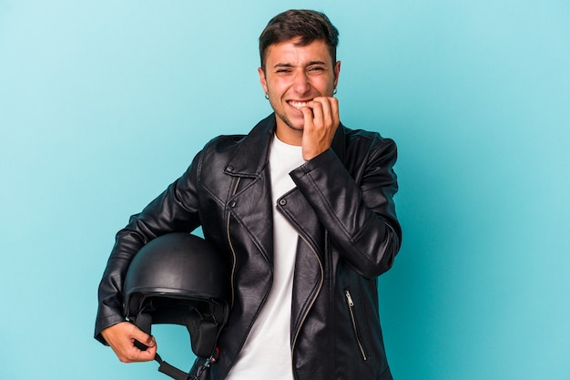 Junge Biker-Mann mit Helm isoliert auf blauem Hintergrund beißende Fingernägel, nervös und sehr ängstlich.