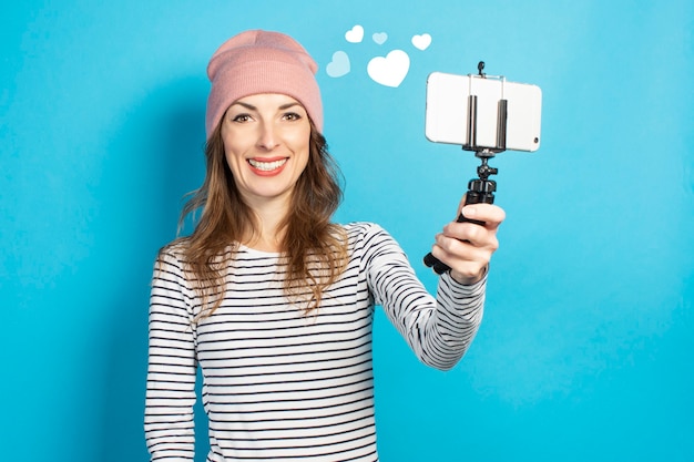 Junge Bloggerin fotografiert sich am Telefon an einer blauen Wand. Konzeptgeschichte, Vlog, Selfie, Blog.