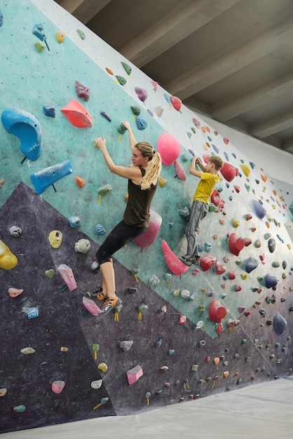 Junge blonde aktive Frau und ihr Sohn in Sportbekleidung Kletterwand mit kleinen künstlichen Steinen beim Training in der Freizeit