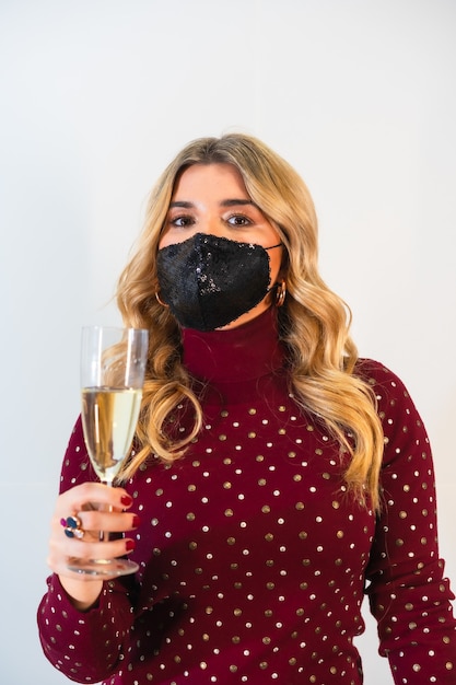 Junge blonde Dame in einer schwarzen Gesichtsmaske, die einen festlichen Toast macht