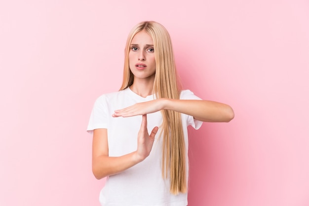 Junge blonde Frau auf der rosafarbenen Wand, die eine Auszeitgeste zeigt.