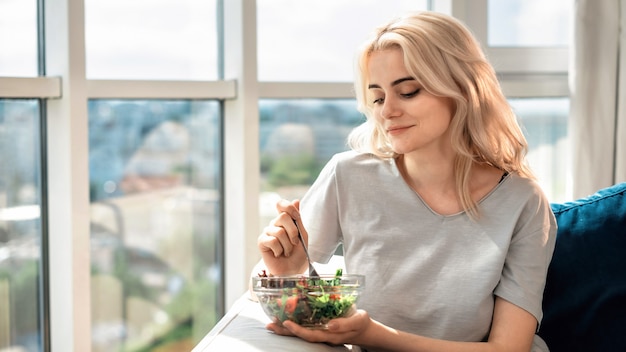 Junge blonde Frau auf einem Sofa mit gesundem grünem Salat